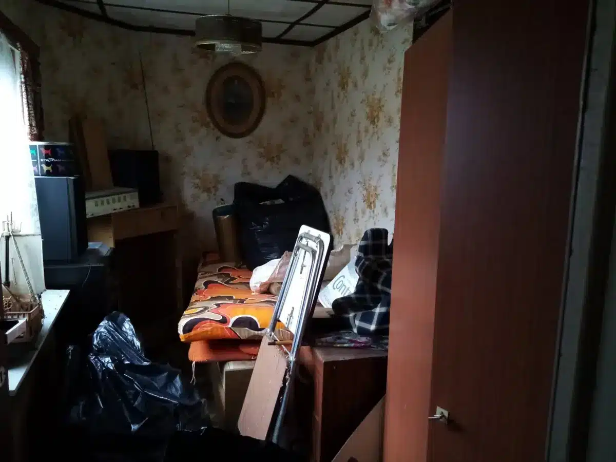 Petite chambre encombrée d'un lit, de sacs et d'objets avant débarras à Rixensart