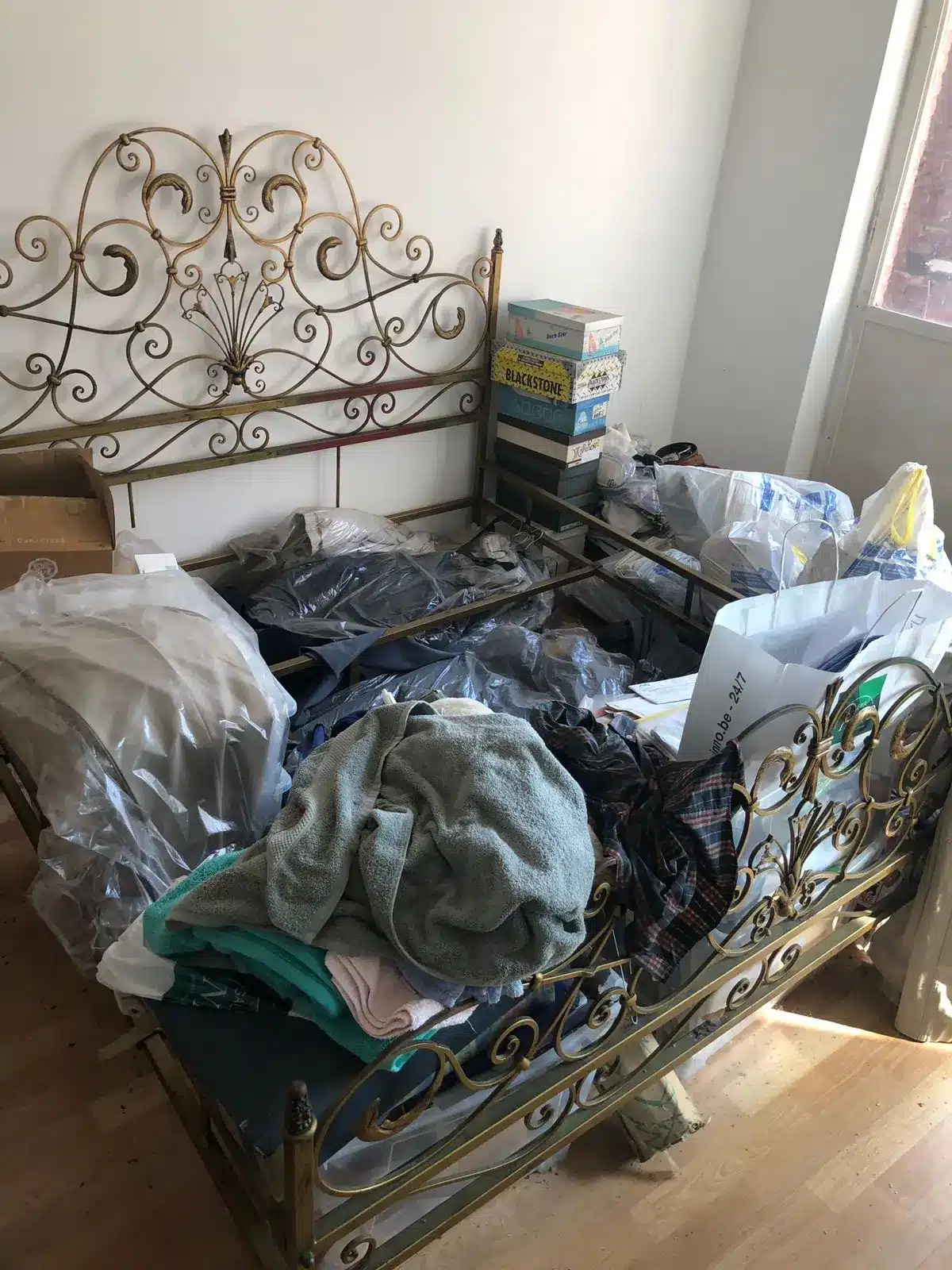 Lit en fer forgé disparaissant sous les vêtements et les sacs avant le tri à Ixelles