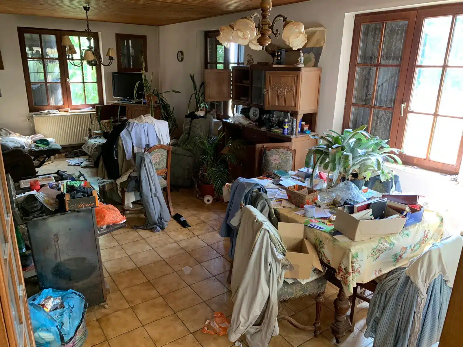 Séjour encombré de vêtements, de cartons et d'objets avant un vide-maison à Nivelles