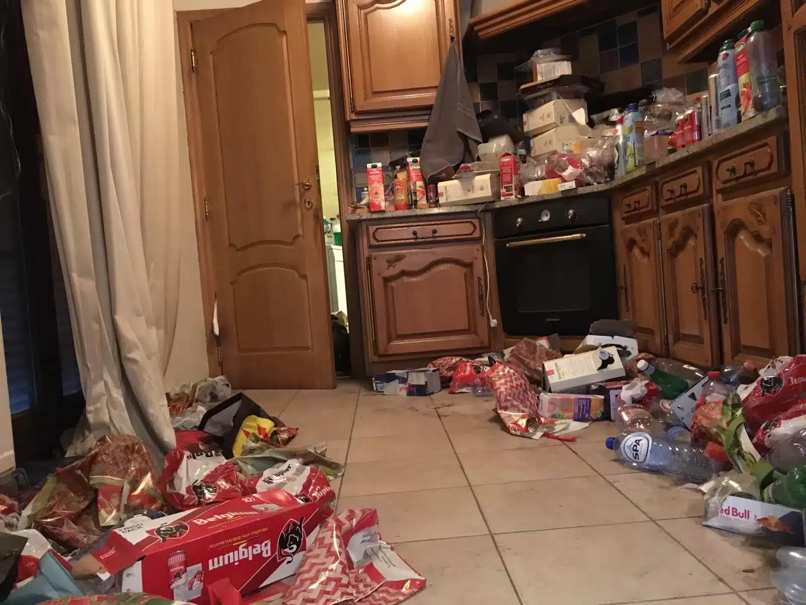 Cuisine au sol couvert d'emballages et de déchets dans une maison encombrée à Obourg