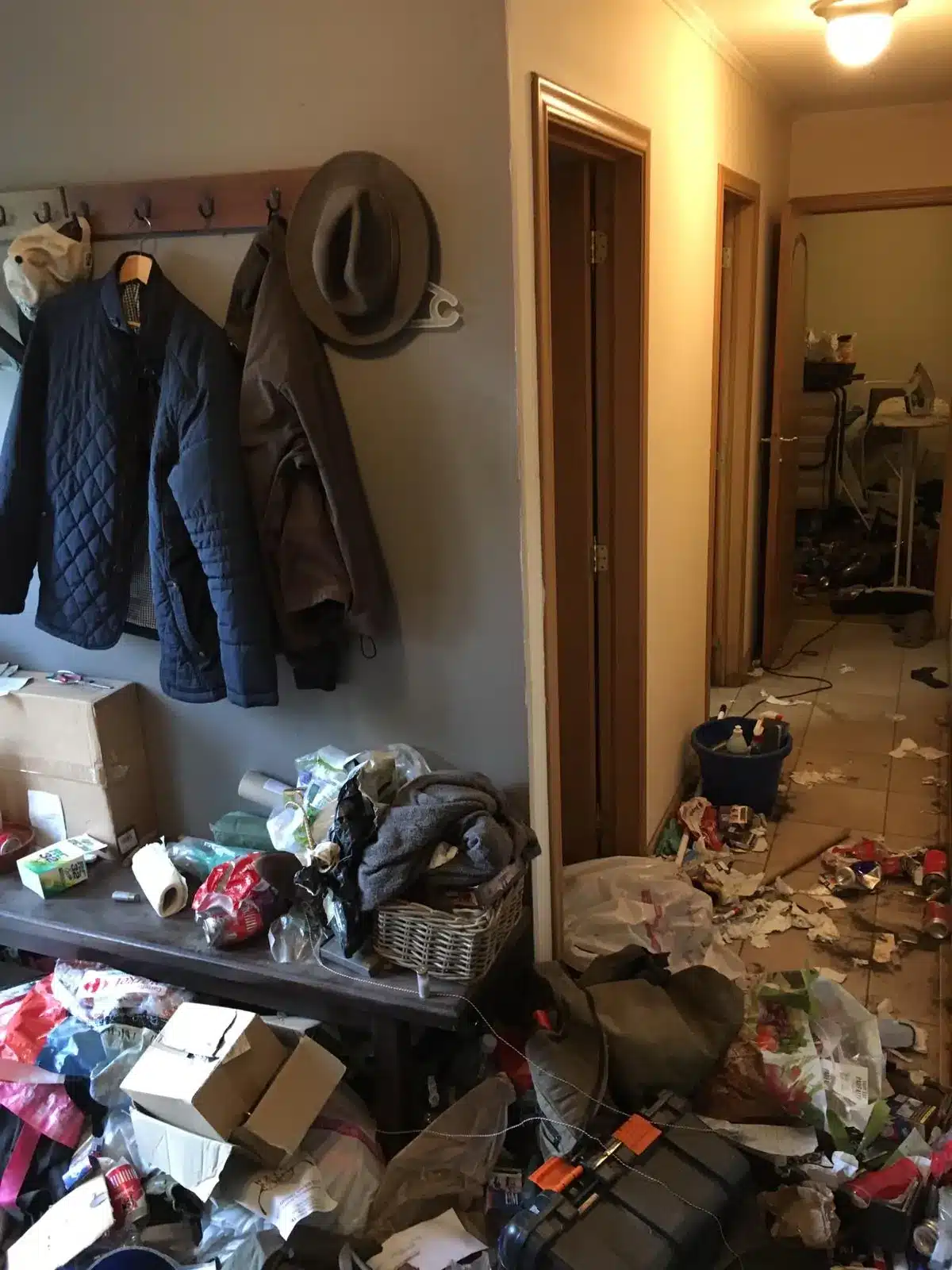 Entrée encombrée de sacs, de vêtements et de déchets avant le nettoyage d'une maison à Obourg