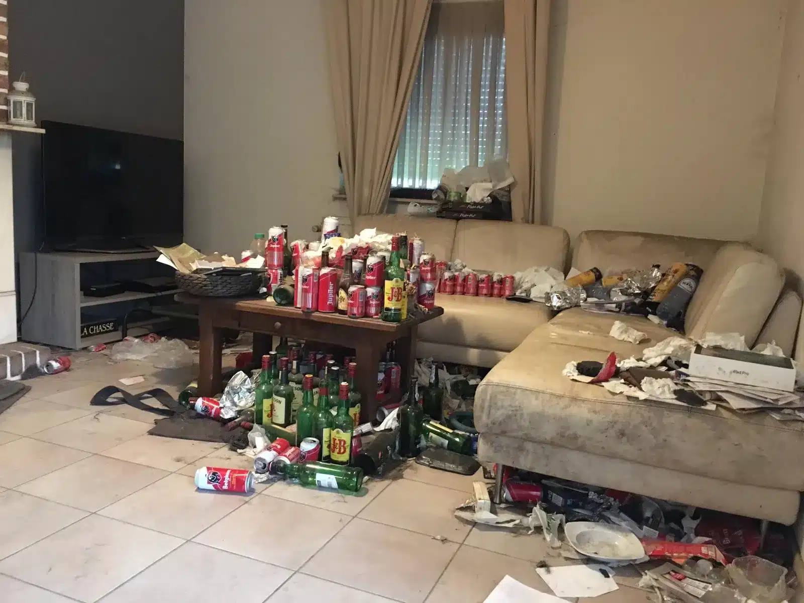 Salon d'une maison à Obourg encombré de canettes, bouteilles et déchets autour du canapé
