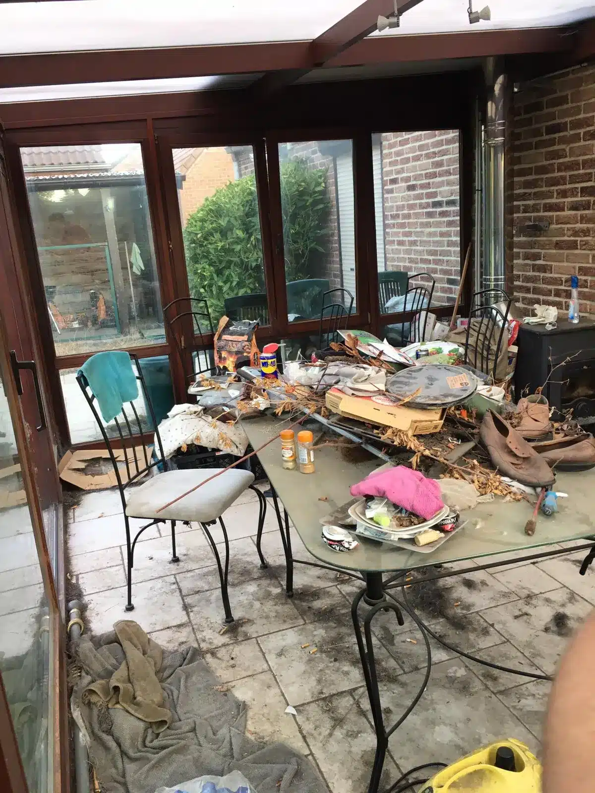 Véranda encombrée d'objets et de déchets sur la table et au sol à Obourg
